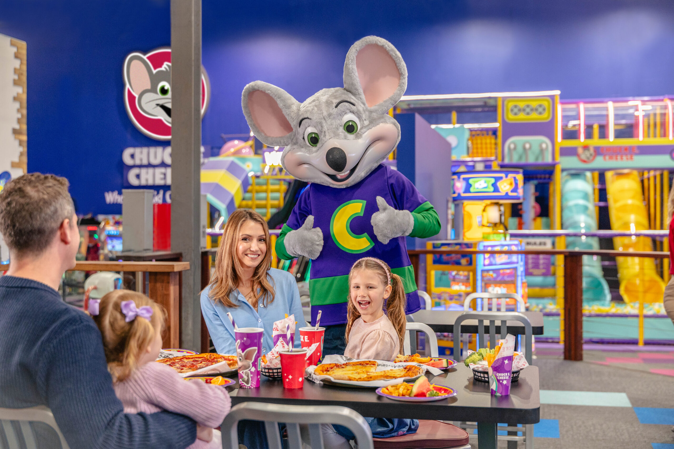 A photo of a family eating at the Chuck E. Cheese restaurant in front of the indoor playground.
